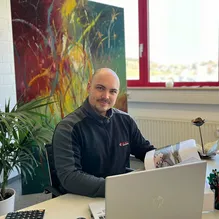 Mitarbeiter am Bürotisch mit Laptop vor einer Sichtschutzwand